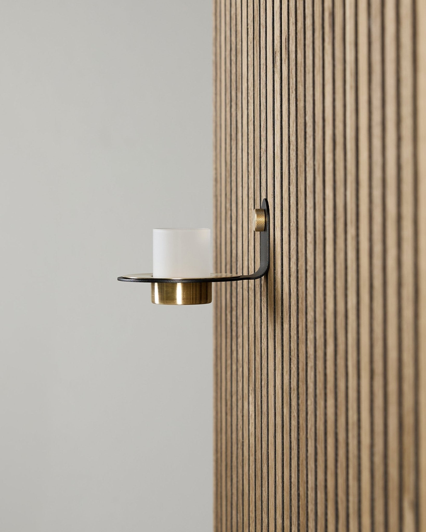 Norr Candle Holder in black en brass van WoodUpp, gemonteerd op een vertical Akupanel Akoestisch paneel, met matglas en brass details.